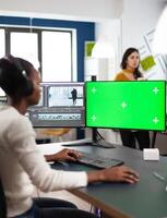 African woman multimedia content creator with headphones processing film montage working at greenscreen, chroma key isolated display of computer. Videographer editing movie in post production software photo