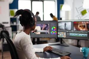 Black woman editor working at project film montage sitting in modern creative agency office. Videographer in digital multimedia company editing movie with post production software photo