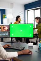 Black woman editor with headphones using with green screen, chroma key mockup computer with isolated display sitting in start-up production studio. African videographer processing film montage photo