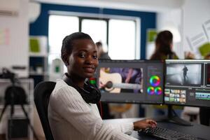 African american editor artist looking at camera smiling editing creative project in post production software working in startup studio office. Videographer editing audio film montage photo