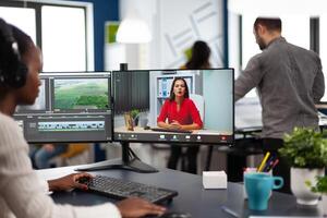 editor in web online conference with project creator on call editing business client work, getting feedback on movie using post production software on two monitors in start up office photo