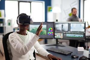 African maker experiencing VR headset, gesturing, editing film montage working at footage and sound on computer with two displays. Videographer processing movie in creative agency photo