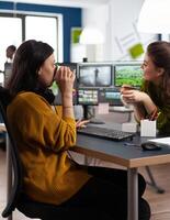Office team of videographers taking work break discussing and laughing, drinking coffee working in montage editing app at pc sitting in digital multimedia company. Creative women editing film photo
