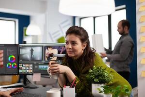 Videographer editing montage of film using modern software sharing ideas with coworker in startup studio office. Coworkers talking about creative process in post production agency photo