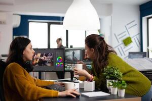 Happy coworkers talking about creative film montage looking at movie production ideas working in start up office with two monitors. Womens editors editing project in post production software photo