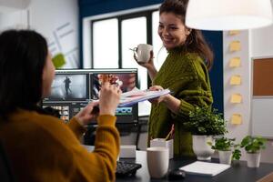 Creators drinking coffee and talking during office break sitting at desk in digital agency studio. editor and sound engineer working at movie project, editing film footage in software app photo