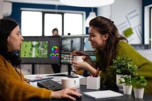 Videographer editing montage of film using modern software sharing ideas with coworker in startup studio office. Coworkers talking about creative process in post production agency photo
