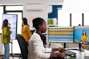 Black retoucher artist analysing images on pc with two monitors and retouching digital assets with stylus pencil. African designer using photo editing software working in creative production office