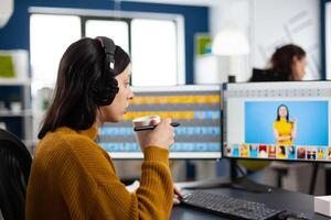 Photographer retoucher with headphones retouching photos using stylus pen drawing on graphic tablet, working at PC with two displays. Creator photo editor working in software app in agency office