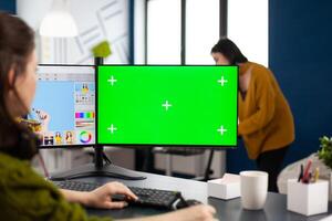 Photo artist retoucher editing assets in digital retouching program working in production agency studio. Photographer woman looking in computer with green screen, chroma key mockup isolated display.