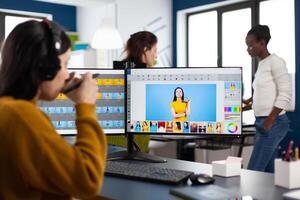 Photographer retoucher with headphones retouching photos using stylus pen drawing on graphic tablet, working at PC with two displays. Creator photo editor working in software app in agency office