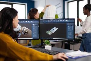 Industrial engineer woman working at pc with two monitors, screens showing CAD software with 3D architecture prototype of gears mechanical piece. Entrepreneur working in creative construction office photo