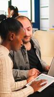 Diverse business people working in teamwork discussing project strategy using laptop sitting on couch at small table. Manager executive analysing financial data from black woman tablet at team meeting photo