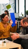 Angry manager woman screaming at diverse employees disagreeing about bad business contract, hitting man with clipboard in head sitting on couch at office desk, conflict dispute about document photo