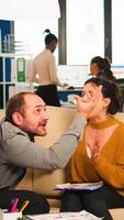 Angry man manager arguing woman employee for bad work result, sitting on couch, while diverse colleagues working scared in background. Business woman employee raging about multitasking difficult job. photo