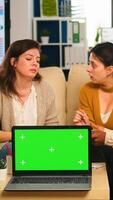Diverse businesswomen analysing annual financial reports sitting on couch in back of laptop with green screen monitor. Leader explainig project strategy using greenscreen pc with chroma key display. photo