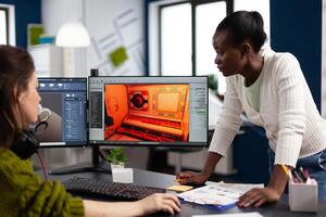 Multiethnic women designer looking at computer with dual displays working together at gaming project in startup office. Gamer workers developing digital games on pc with modern technology photo