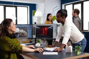 Multiethnic women designer looking at computer with dual displays working together at gaming project in company office. Gamer workers developing new games application on pc with modern technology photo