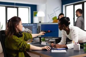 Diverse women game developers creating game interface sitting in startup creative production company pointing at pc displays. Workers developing online graphics games with modern technology photo