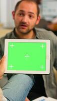 Over the sholder of manager woman sitting on couch talking with coworker holding tablet with green screen while diverse team working. Multiethnic people planning project on chroma key display photo