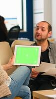 Back view of businesswoman sitting on couch using tablet with green screen talking with colleague while team working on background. Multiethnic coworkers planning project on chroma key display photo