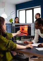 Diverse women game developers creating game interface sitting in startup creative production company pointing at pc displays. Workers developing online graphics games with modern technology photo