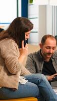 Man colleague asking woman manager about graphics information while she is talking on smartphone. Multiethnic creative coworkers planning new financial project working in open plan office photo