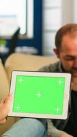Business people sitting on couch analysing financial statistics, holding tablet with green screen while diverse team working on background. Multiethnic coworkers planning project on chroma key display photo