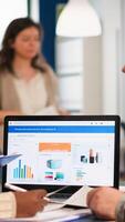 Busy multicultural, diverse employees analysing annual financial statistics sitting at desk in front of laptop holding documents searching business solutions. Team of businesspeople working in company photo