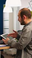 Enthusiastic diverse businesspeople reading annual financial report sitting at table in modern startup business office holding tablet and smiling. Team of multiethnic businesspeople working in company photo