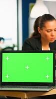 Laptop with green screen ready for presentation placed on desk while business people work in background. Group of employees using notebook with chroma key display. mock up monitor photo