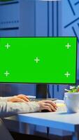 Businesswoman looking at green screen monitor of computer sitting at desk in business office late at night. Freelancer watching desktop monitor display with green mockup, chroma key working overtime. photo