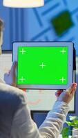 Businesswoman holding tablet with green screen monitor sitting at desk in business office late at night. Freelancer watching desktop monitor display with green mockup, chroma key working overtime. photo
