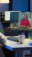 Freelancer working remotely discussing with woman partner online sitting in front of computer in start-up office talking during virtual meeting at midnight, using wireless headphone doing overtime photo