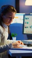 Exhausted manager trying to finish business project respecting deadline working at night in front of computer taking notes writing on notebook. Tired employee overtime sitting at desk in workplace photo