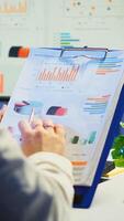 Close up of business woman holding clipboard with graphics and financial statistics working overtime in front of computer sitting in start-up business office. Busy employee using modern technology photo