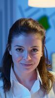 Close up portrait of business woman smiling at camera after reading mails on laptop sitting at desk in start-up company late at night. Focused employee using technology network wireless doing overtime photo