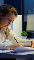 Overworked woman architect analysing and matching blueprints sitting at desk in front of computer late at night. Designer using arhitecture plans of buildings working overtime, creating and studying photo
