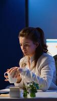 Business woman working overtime checking team project, taking notes, drinking coffee, analysing financial documents sitting at desk in start-up company late at night using modern technology network photo
