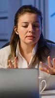 Business woman using wireless headphone duing conference working overtime from start-up office in front of laptop. Lady using modern technology network talking on virtual meeting at midnight photo