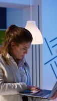 Busy entrepreneur analysing financial reports standing in start up office late at night holding laptop. Focused employee using technology network wireless doing overtime reading writing, searching photo