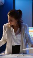 Stressed manager woman working with financial documents checking graphs, holding papers, reading raports, standing at desk late at night in start-up office doing overtime to respect deadline. photo