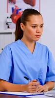 Medical assistant typing on laptop and taking notes on clipboard in hospital office. Healthcare physician in medicine uniform writing list of consulted, diagnosed patients, making research. photo