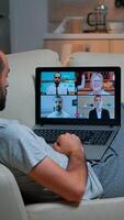 Comfortable man relaxing on couch while having online business conference with collegues using laptop computer during quarantine. Focused adult talking on videocall use webcam late at night in kitchen photo