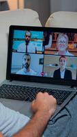 Over shoulder view of man in pajamas having online conversation with teammates working at online technology project using laptop computer, videoconference web internet communication photo