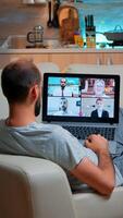 Caucasian male talking with collegues during call conference using laptop computer with modern technology wireless. Tired man relaxing on sofa late at night in kitchen photo