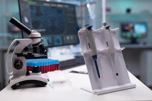 Nobody in research laboratory with micro pipette on desk. Empty scientific development room with professional equipment, microscope and lab glassware. Biochemistry cabinet with tools photo