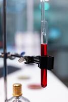 Close up of test tube with blood on dripping pipe in science laboratory. Chemical glassware flask with red liquid and solution on lab desk. Biochemistry workplace with instruments photo