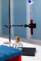 Chemical dripping pipe with test tube in science laboratory at clinic. Close up of microbiology lab with vacutainers and chemistry instruments, flask filled with red substance for analysis photo
