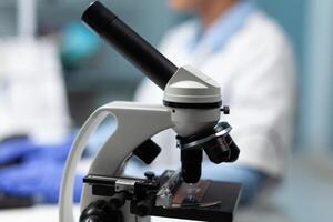 Selective focus on medical microscope standing on table in biochemistry hospital laboratory. Specialist doctor typing medicine expertise working at microbiology experiment. Microscope glass sample photo